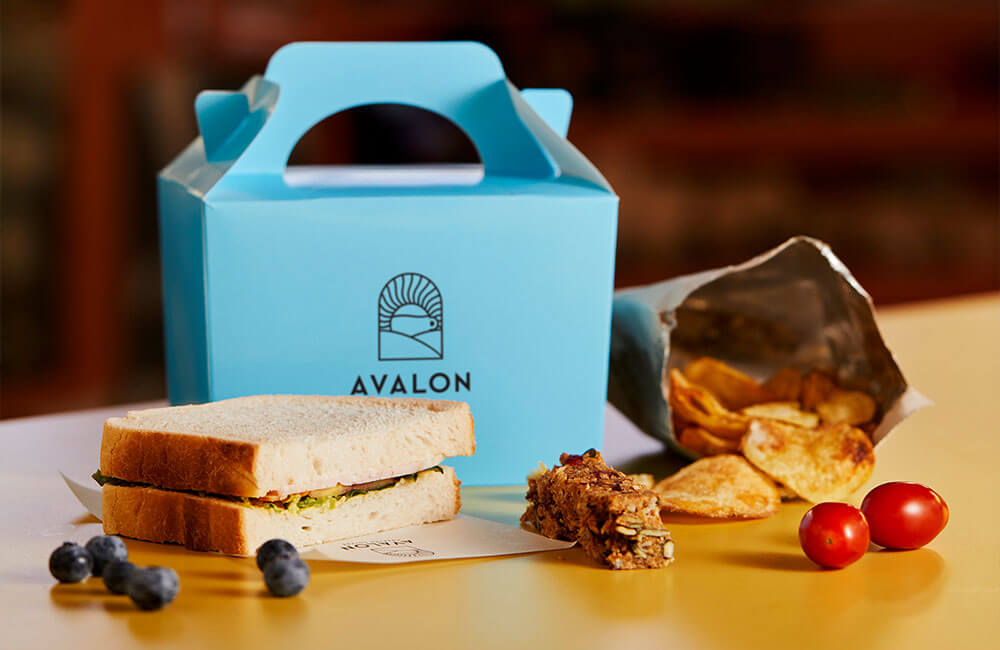 An Avalon lunch box with a sandwich, crisps, flapjack and fruit
