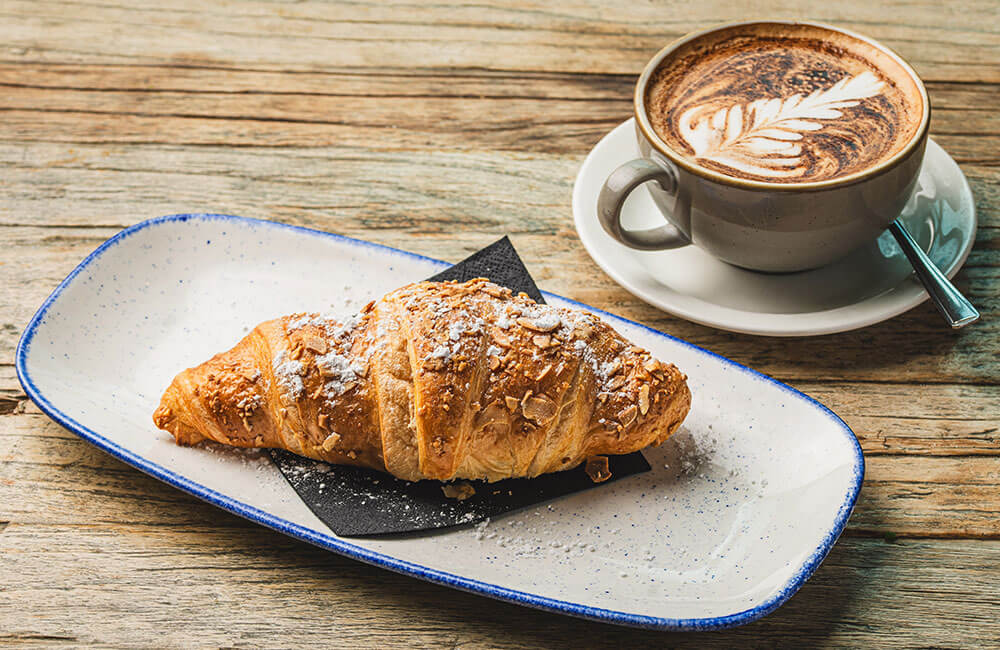 An almond croissant with a flat white
